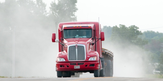 Red semi with flatbed trailer driving with dust rising up behind