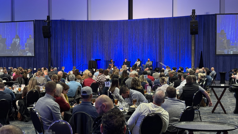 Room of people and panel discussion taking place on stage
