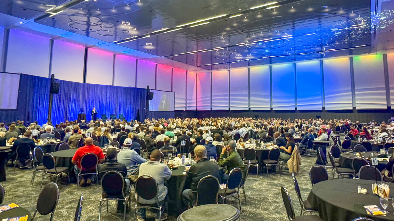 Large room full of people sitting at tables and presentation stage
