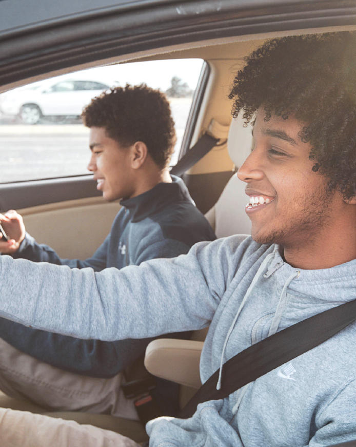 Two young men wearing their seatbelts in the front seat of a car.