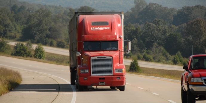 Red semi truck driving around a curve toward the viewer