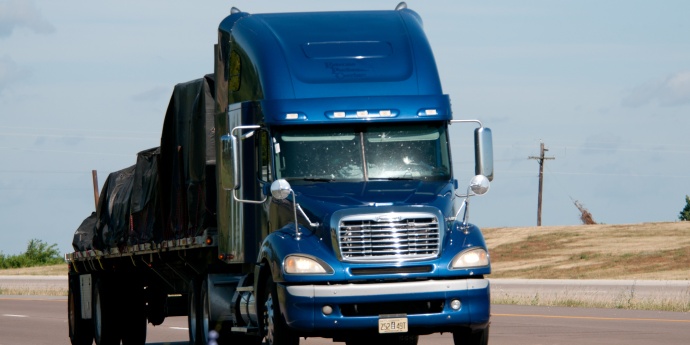 A dark blue semi truck pulls a covered load on a flatbed trailer