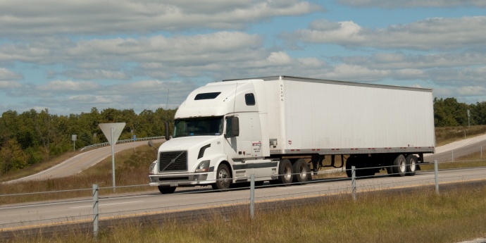 A white tractor trailer drives under a blue cloudy sky