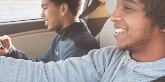 Two young men wearing their seatbelts in the front seat of a car.