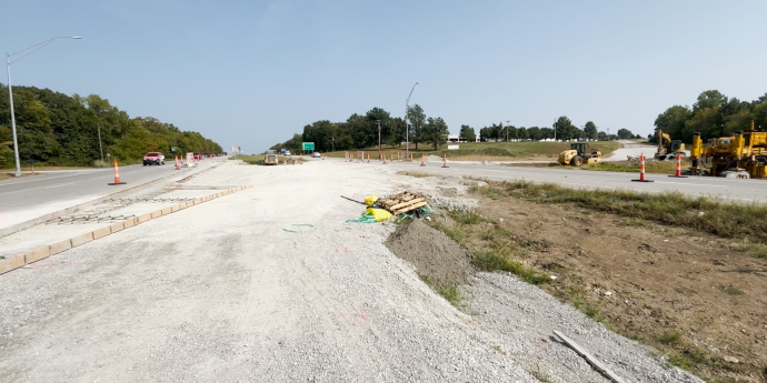 Roadway construction area between two roadways with gravel, various cones, and construction equipment in the area