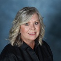 Photo of blonde woman in dark colored shirt on blue background.