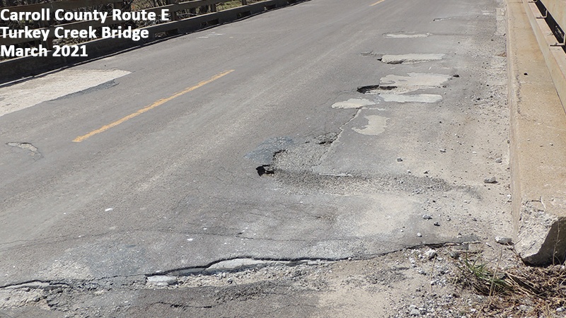 Photo showing deterioration, potholes and repaired potholes on the asphalt driving surface of the Carroll County Route E Turkey Creek Bridge