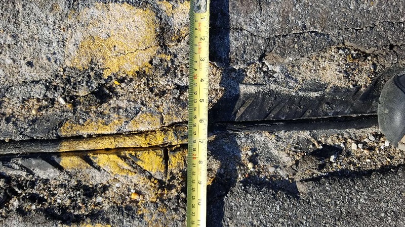 A close up photo of a deteriorating expansion joint, measuring tape across the joint, and the toe of a boot on the right of the photo on the north end of the Carroll County US Rte 24 Bridge over OR 24 and BNSF RR