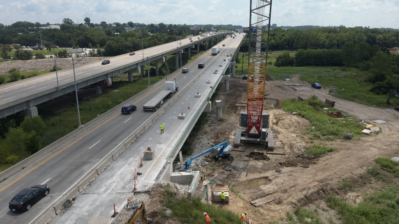 Aerial view of highway bridge partially under construction with a crane on one side and another highway bridge on the other